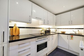 Uma cozinha moderna com armários brancos, bancada preta e forno embutido.