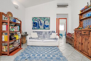 Een woonkamer met een witte bank, een blauw gestreept tapijt, een boekenkast, een schilderij van dieren en een houten kast.