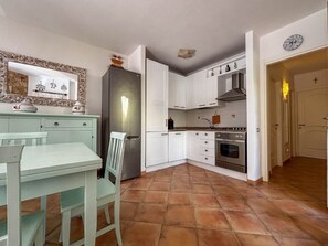 Cocina compacta con armarios blancos, horno integrado y comedor con mesa y sillas.