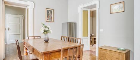 Un comedor con una mesa y sillas de madera, un jarrón con flores, un refrigerador y un armario de madera.