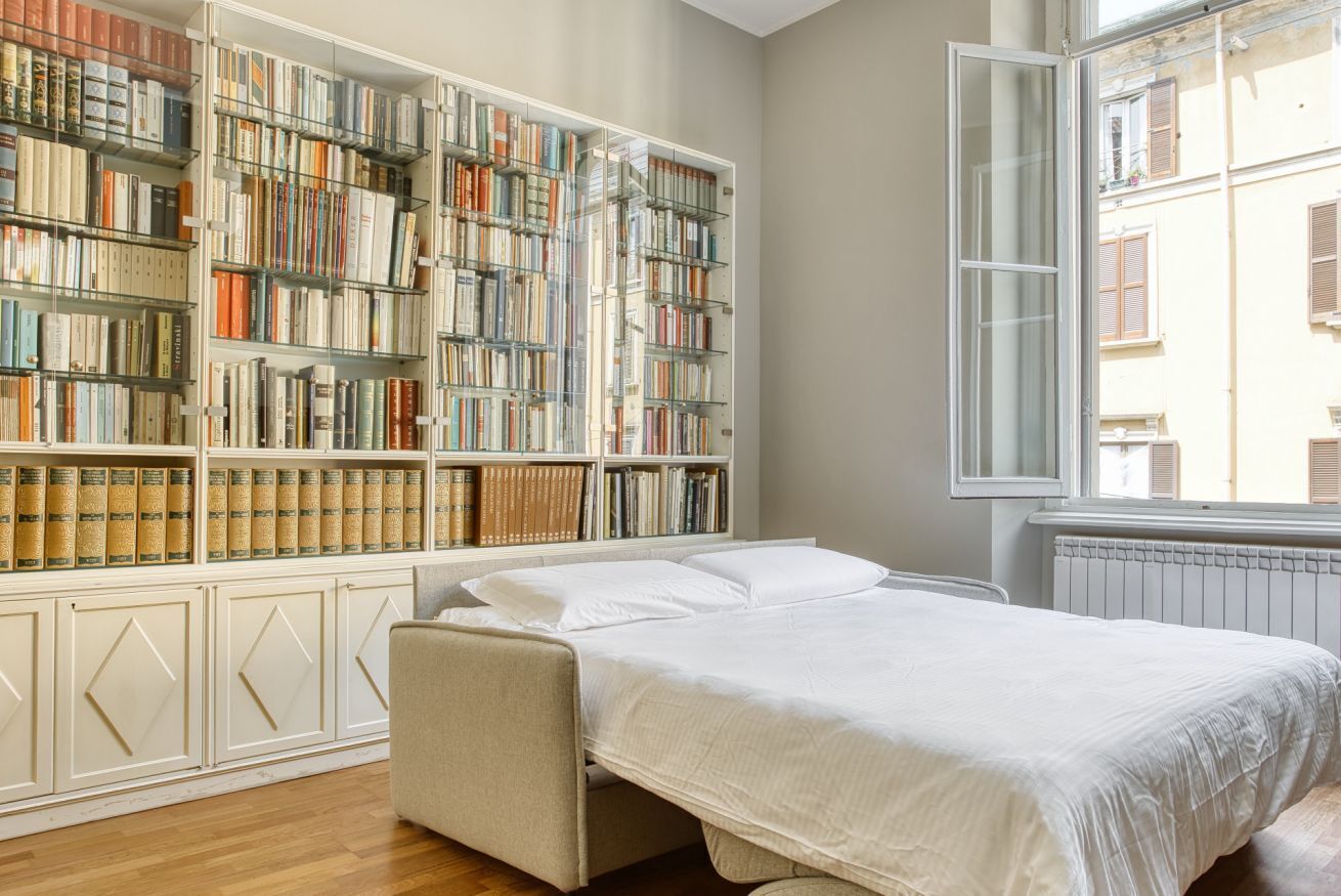Een slaapkamer met een grote boekenkast, een bed en een raam.