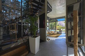 Un intérieur moderne avec un escalier, une plante en pot et une vue sur un espace extérieur aménagé pour s’asseoir.