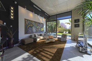 Un salon moderne avec un grand tableau abstrait, un canapé d’angle et une porte vitrée donnant sur un espace extérieur.