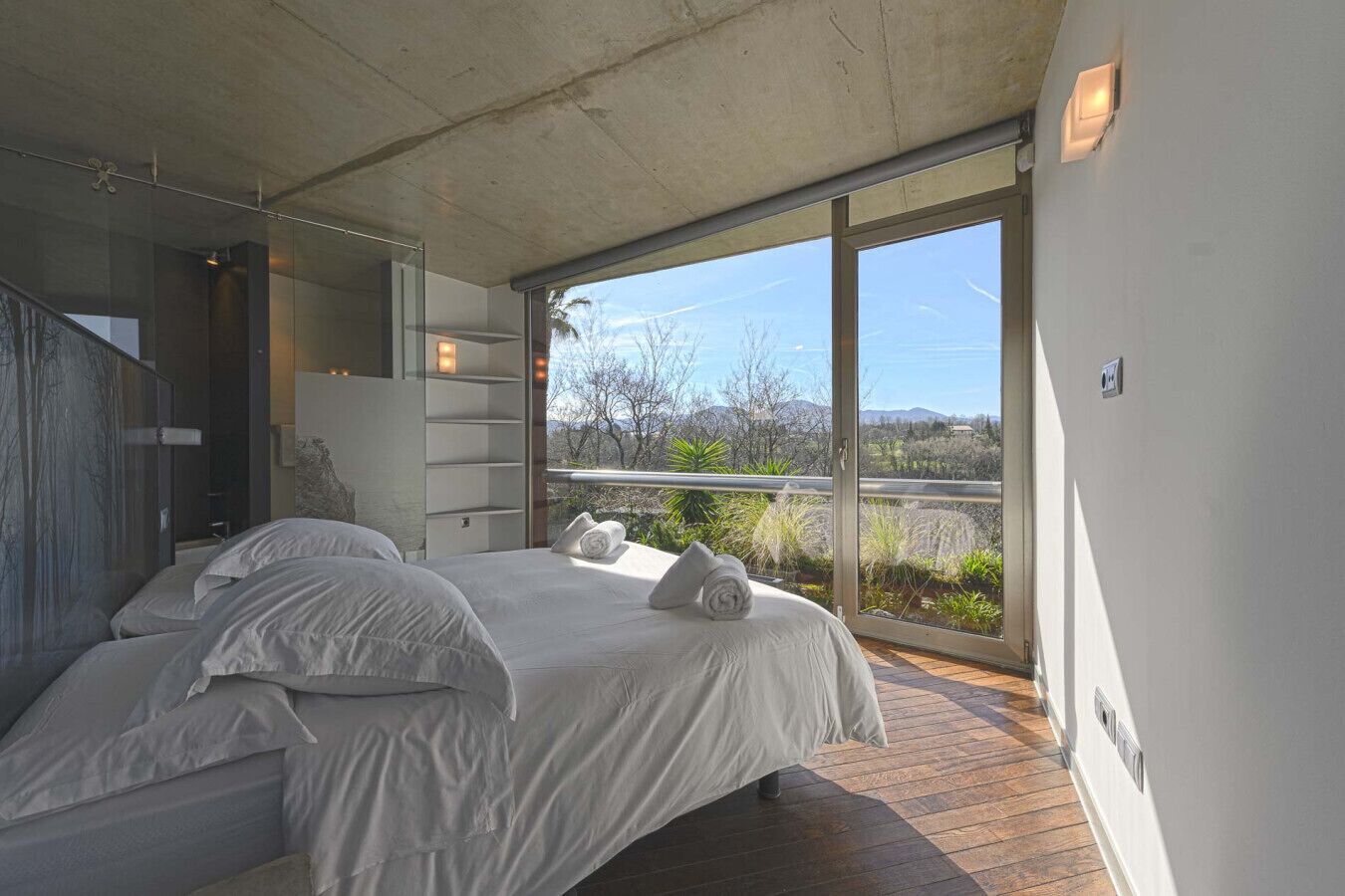 Een moderne slaapkamer met een groot bed, een glazen deur naar een balkon en uitzicht op de omgeving.