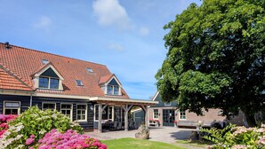 Et traditionelt hus med rødt tegltag, en overdækket terrasse og en velholdt have med lyserøde blomster.