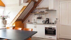 Een keuken met witte kasten, een houten plafond en een eettafel met oranje stoelen.