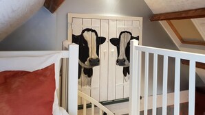 Een slaapkamer met een wit kinderbedje, een houten plafond en een deur met een koeien schilderij.