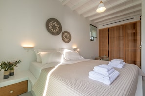 A bedroom with a large bed, two wall-mounted lamps, a wooden wardrobe, and a potted plant. - Phos Villas Tinos (Tinos)