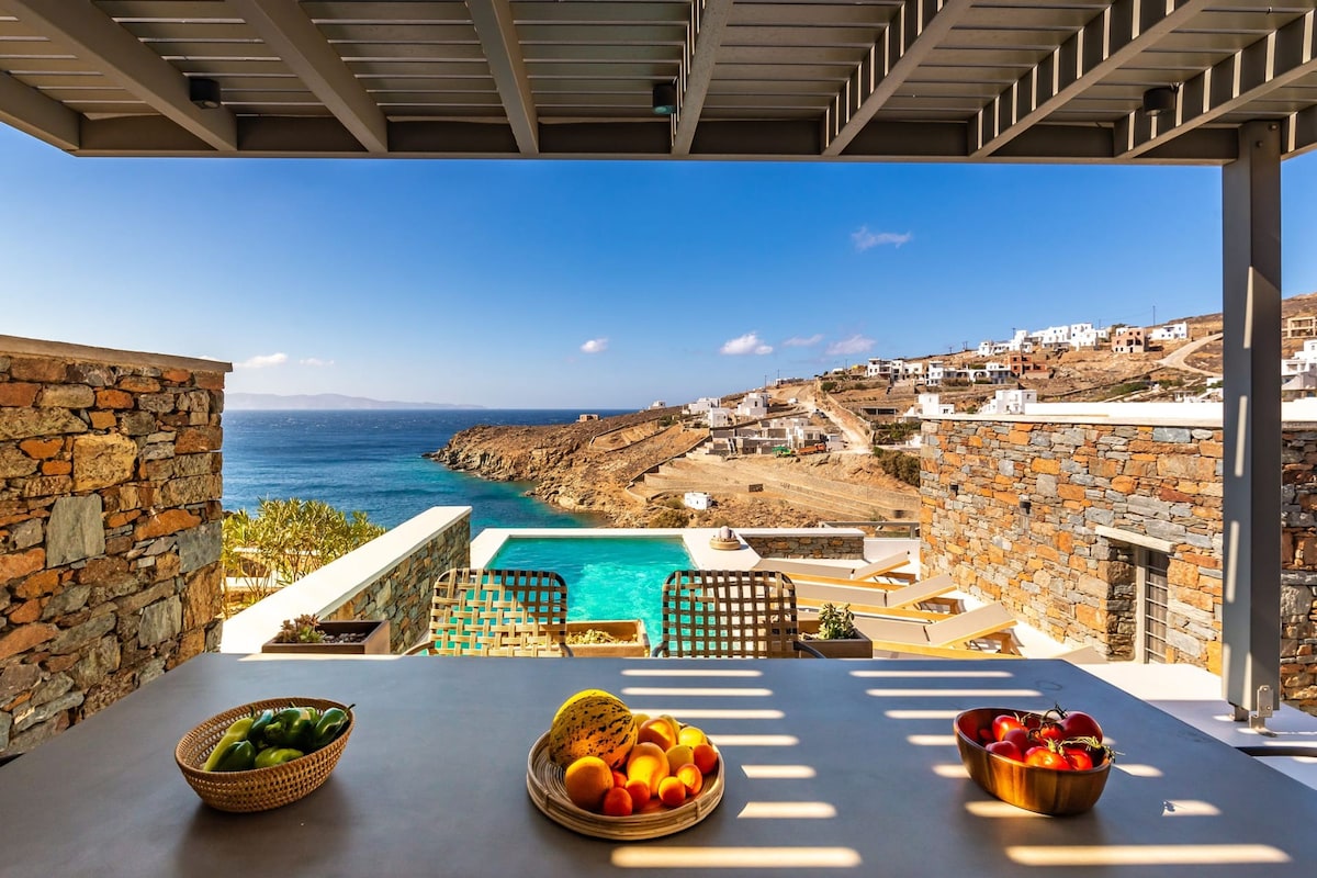 Une terrasse avec une piscine, des murs en pierre et une vue sur la mer et les bâtiments situés sur la colline.