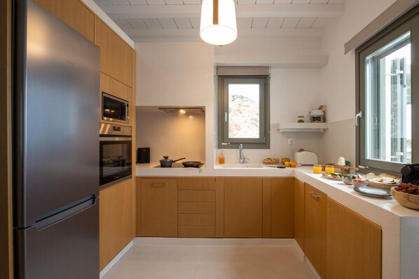 Una cocina moderna con armarios de madera, un refrigerador de acero inoxidable, un microondas y un ventanal que proporciona luz natural.