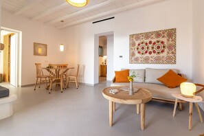 A modern living room with a dining area, a sofa with orange cushions, a coffee table, and a wall-mounted artwork.