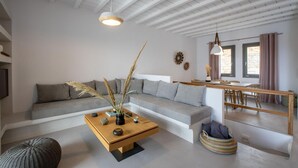 A modern living room with a grey sofa, a wooden coffee table with decorative items, a woven pouf, and a dining area with a wooden table and chairs.