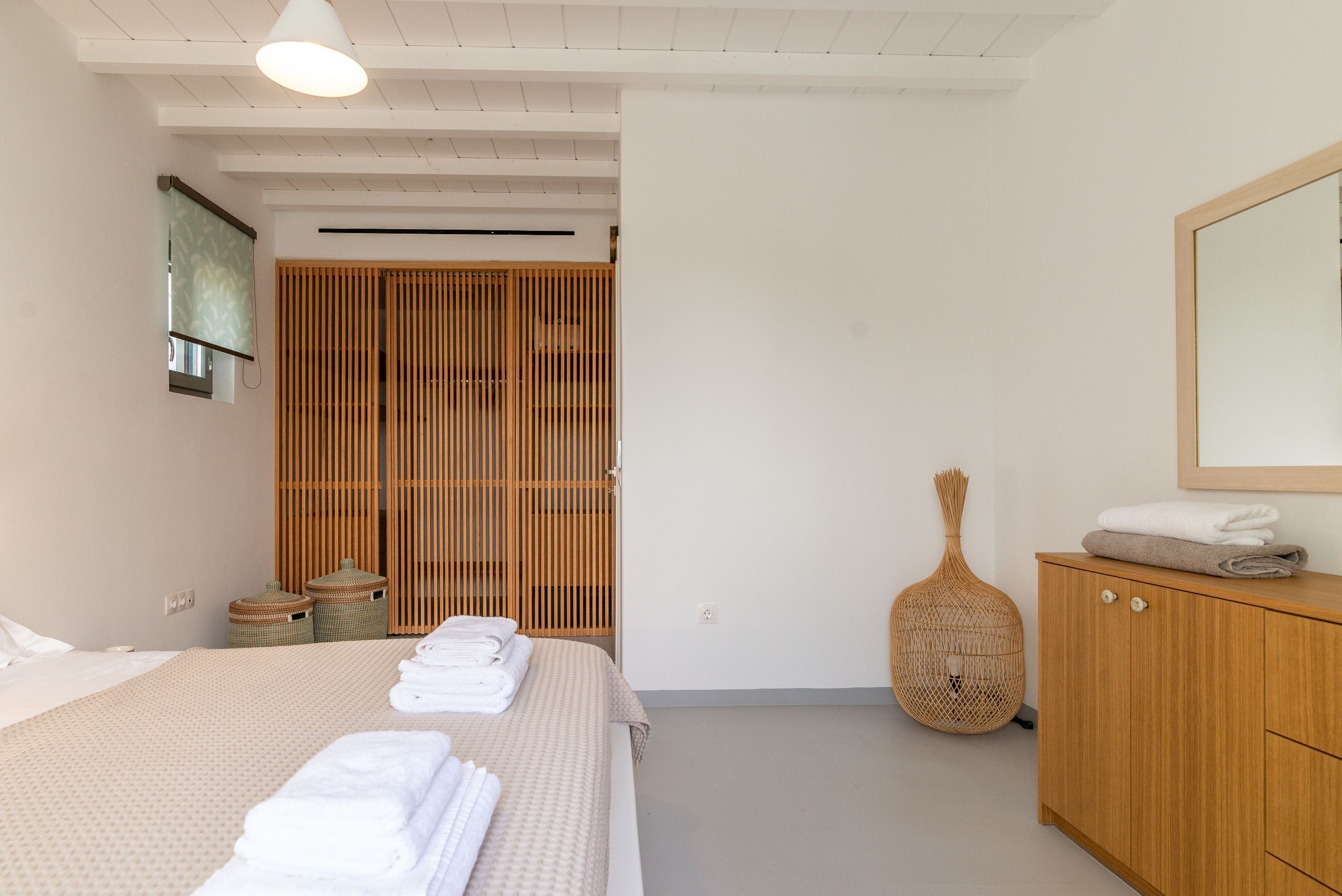 Ein Schlafzimmer mit einem Bett, einem Holzschrank, einem Korbwäscheschrank und einem Spiegel an der Wand.