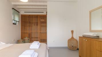 Ein Schlafzimmer mit einem Bett, einem Holzschrank, einem Korbwäscheschrank und einem Spiegel an der Wand.