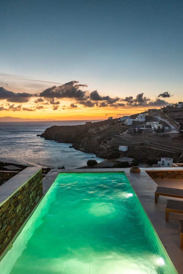 A pool with a view of the sea and a coastal village at sunset. - Phos Villas Tinos (Tinos)