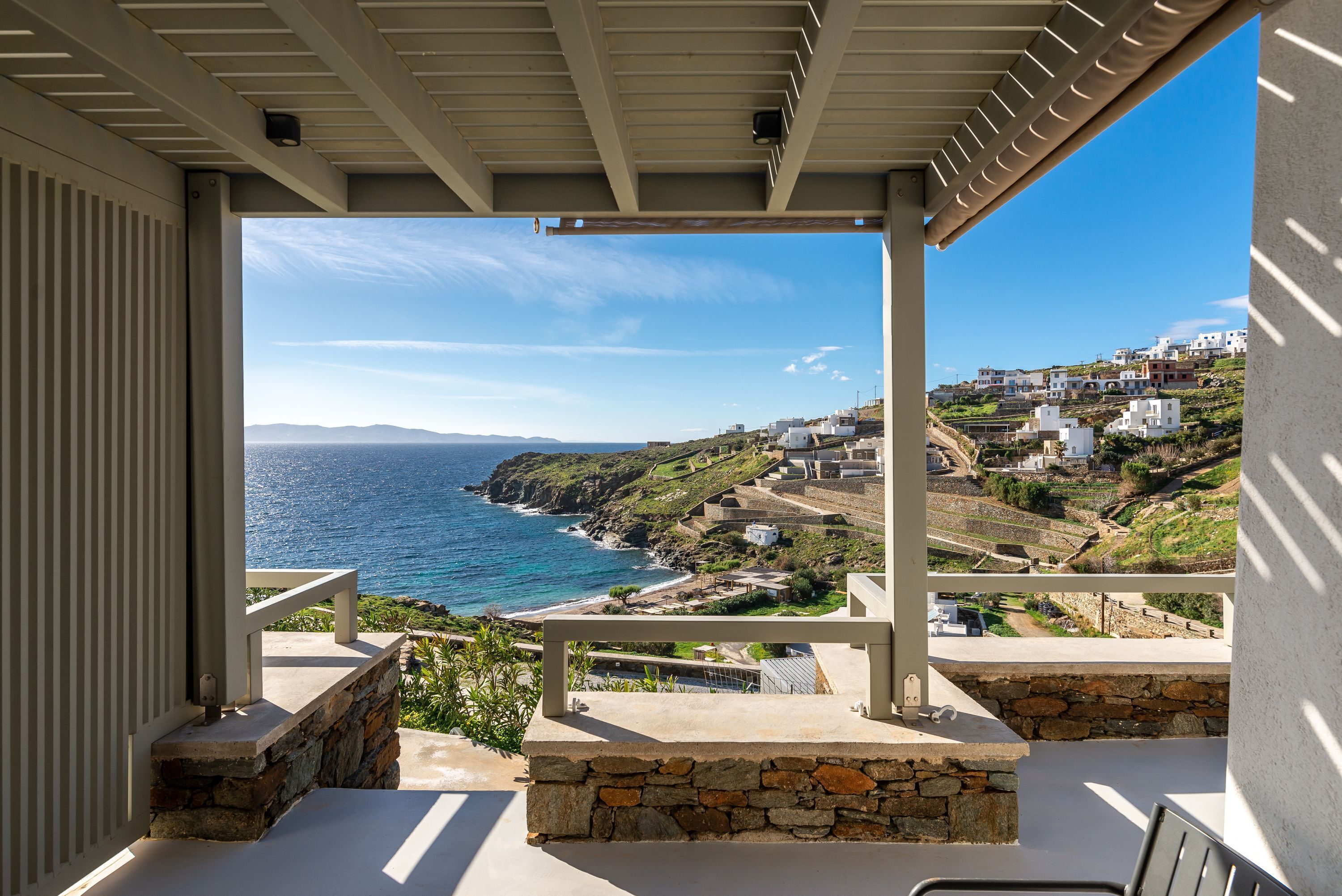 A balcony with a stone ledge, a view of the ocean, and buildings on a hillside.