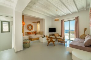 A modern living room with a sofa, a TV, and a balcony with a view. - Phos Villas Tinos (Tinos)