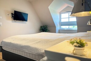 A bedroom with a bed, a TV mounted on the wall, a window, and a desk with a plant. - Baltischer Hof 53 Apartment (Ostseebad Boltenhagen)