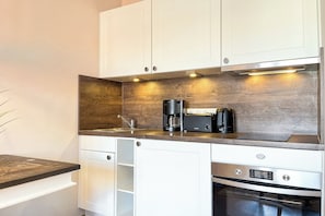 Eine moderne Küche mit weißen Schränken, einer Holzrückwand, einer Kaffeemaschine und einem Backofen.
