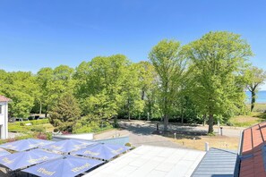 Ein Innenhof mit mehreren blauen Sonnenschirmen, Bäumen und einem Gebäude mit rotem Dach.