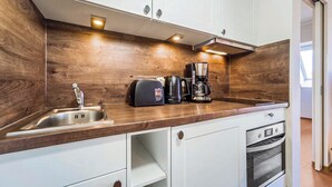 A compact kitchen with a wooden backsplash, a sink, a coffee maker, and a built-in oven.