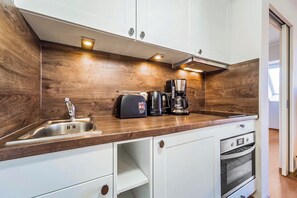 A compact kitchen with a wooden backsplash, a sink, a coffee maker, and a built-in oven.