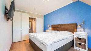 A bedroom with a bed, bedside lamps, a TV mounted on the wall, and a wardrobe.