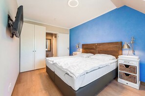 A bedroom with a bed, bedside lamps, a TV mounted on the wall, and a wardrobe.