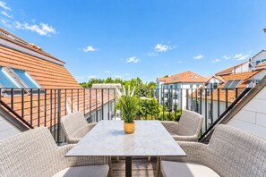Eine Dachterrasse mit Tisch und Stühlen, einem Blumentopf und Blick auf die Nachbargebäude.
