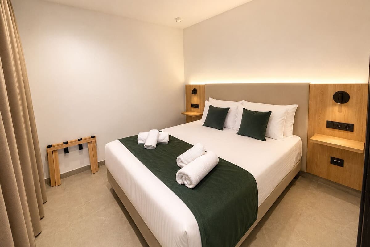 A hotel room with a large bed, two bedside tables, a wooden nightstand, and a wall-mounted light fixture.
