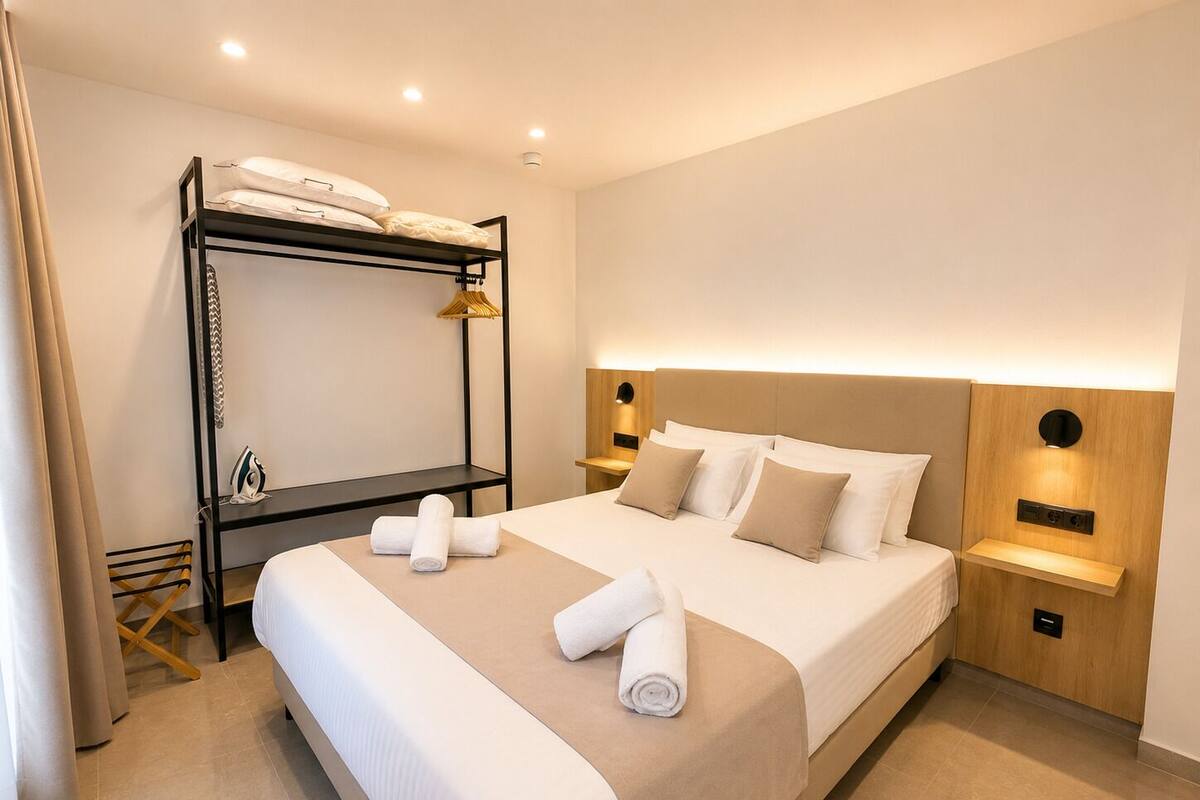 A modern hotel room with a bunk bed, a large bed with a headboard, bedside tables, and a wall-mounted light fixture.