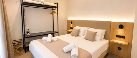 A modern hotel room with a bunk bed, a large bed with a headboard, bedside tables, and a wall-mounted light fixture.