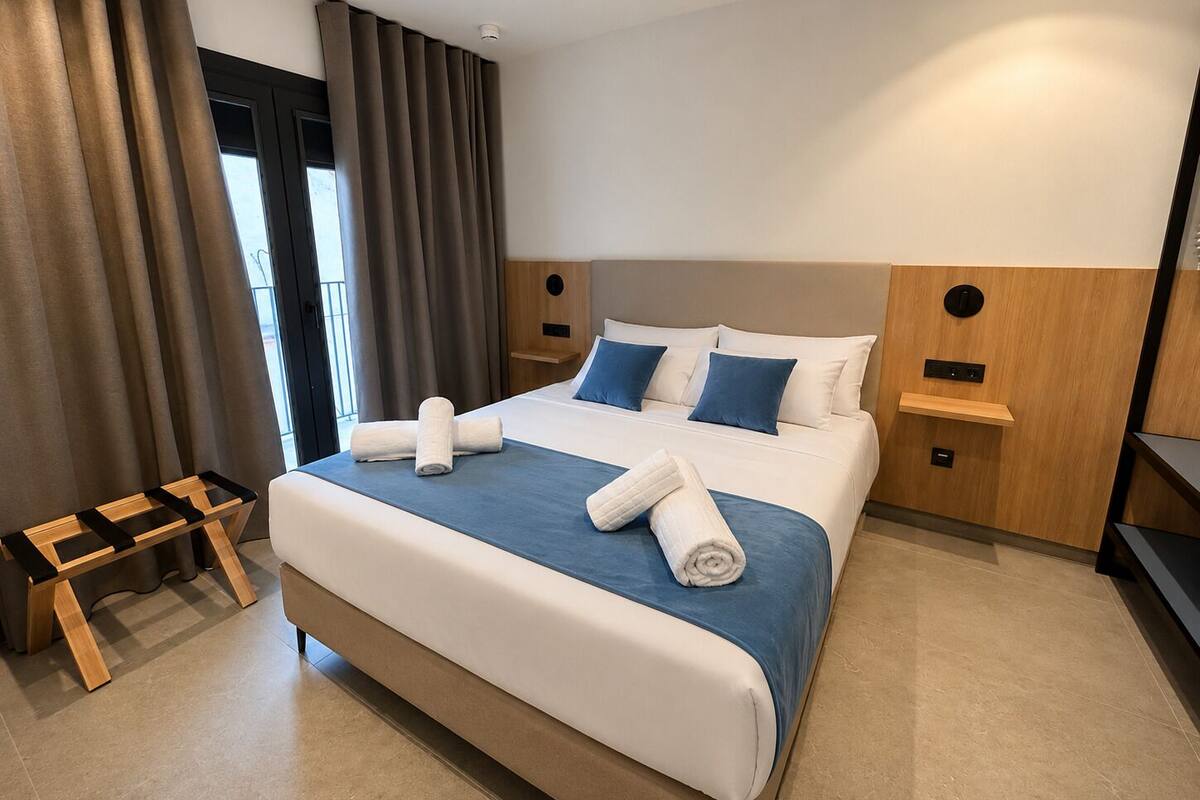 A hotel room with a large bed, two bedside tables, a wooden bench, and a view of the outdoors.