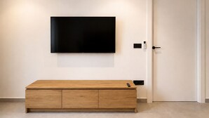 A modern room with a flat-screen TV mounted on the wall, a wooden console table, a door, and a wall-mounted thermostat.