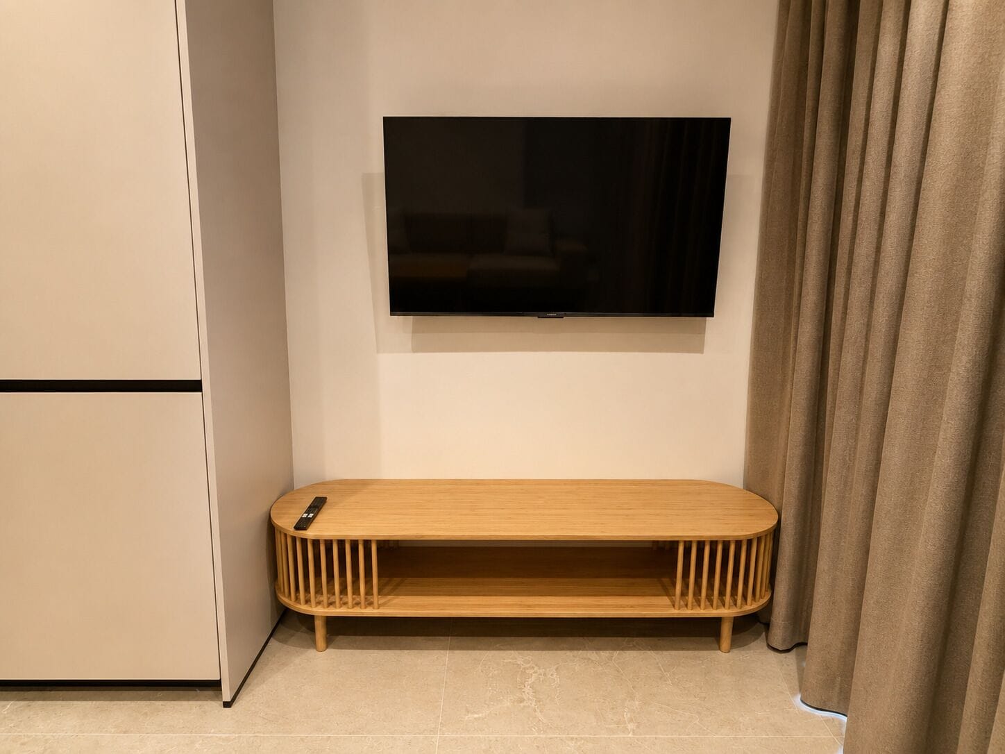 Een moderne woonkamer met een flatscreen televisie aan de wand, een houten tv-meubel en een gordijn.