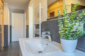 Ein modernes Badezimmer mit einem weißen Waschbecken, einem chromfarbenen Wasserhahn und einer Topfpflanze.