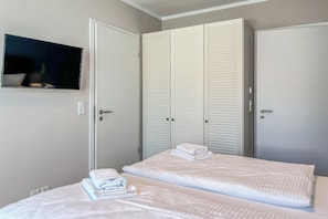 Ein Hotelzimmer mit zwei Betten, einem an der Wand befestigten Fernseher und weißen, verstellbaren Schränken.