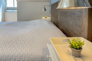 A neatly made bed with a quilted white cover, a bedside table with a lamp, and a small potted plant. - Baltischer Hof apartment 64 (Ostseebad Boltenhagen)