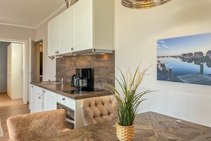 Een moderne keuken met witte kasten, een houten aanrecht en een koffieapparaat. Er is een eethoek met een houten tafel en stoelen, en een potplant op de tafel.