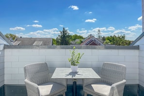A rooftop terrace with a table and two wicker chairs, a potted plant, and a view of surrounding buildings. - Baltischer Hof apartment 64 (Ostseebad Boltenhagen)