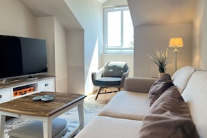 A modern living room with a flat-screen TV, a wooden coffee table, a sofa, and a chair. - Baltischer Hof apartment 64 (Ostseebad Boltenhagen)