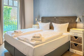 Ein ordentlich bezogenes Doppelbett mit weißen Leinen und Handtüchern, ein Holz-Kopfbrett, Nachttischlampen und ein Nachttisch mit Korbwannen.