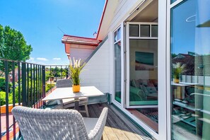 Ein Balkon mit Tisch und Stühlen, einer Topfpflanze und einer Glastür, die zu einem Zimmer mit einem Bett und einem Sessel führt.