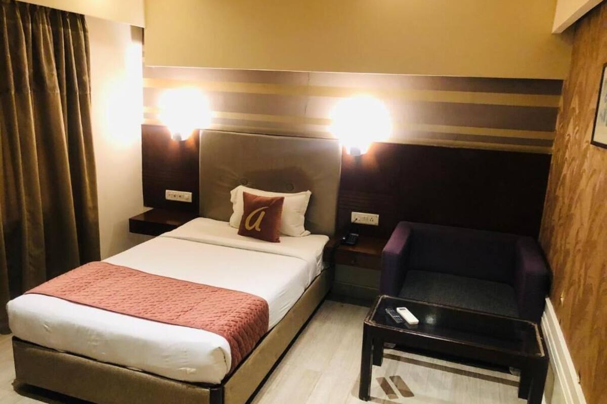 Habitación de hotel con cama, una silla, mesita de noche y lámpara.