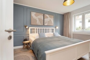 Ein Schlafzimmer mit einem weißen Bett, einem kleinen Holzschemel, einem runden Teppich und zwei Wandleuchten.