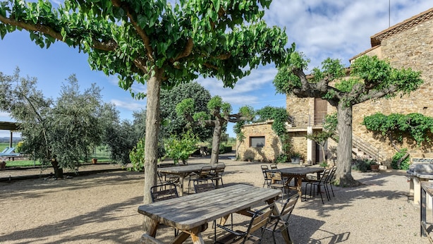 Une terrasse extérieure avec des tables et des chaises, entourée d’arbres et d’un bâtiment en pierre.
