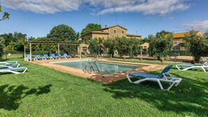 Un espace piscine avec des chaises longues, une pergola et un bâtiment en pierre en arrière-plan.