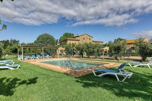 Zona de piscina con sillones de descanso, una pérgola y un edificio de piedra al fondo.