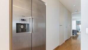 Una cocina moderna con un refrigerador de acero inoxidable, piso de madera y un pasillo visible que conduce a un dormitorio.