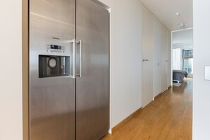 A modern kitchen with a stainless steel refrigerator, wooden flooring, and a visible hallway leading to a bedroom. - Asterie B 0301 met garage (Nieuwpoort)